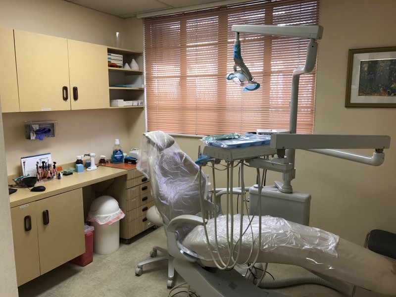 A dental clinic with beige dental chair and yellow cabinets and drawers