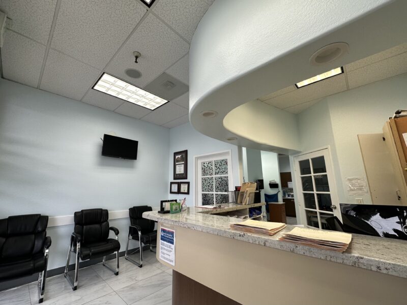 A clinic lobby with three black chairs and brown counter